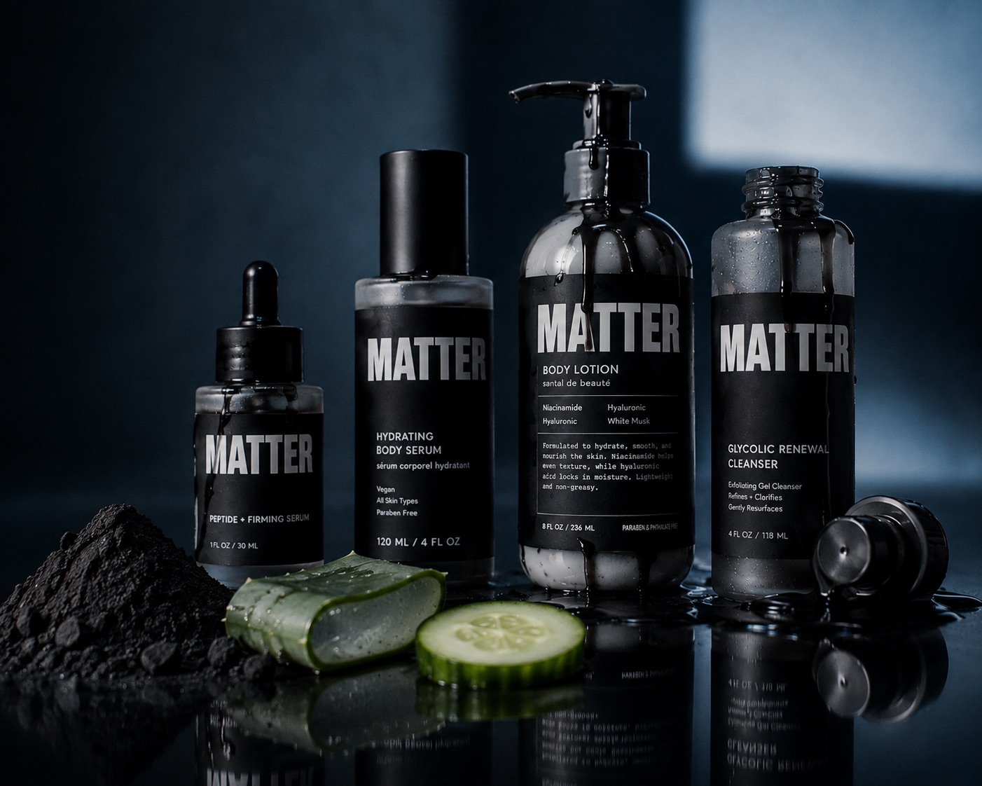 Four matte black MATTER bottles on a wet reflective surface with charcoal powder, aloe and cucumber slices