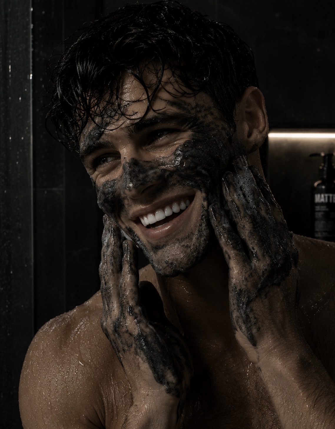 Man in the shower lathering black MATTER charcoal cleanser onto his face, grinning